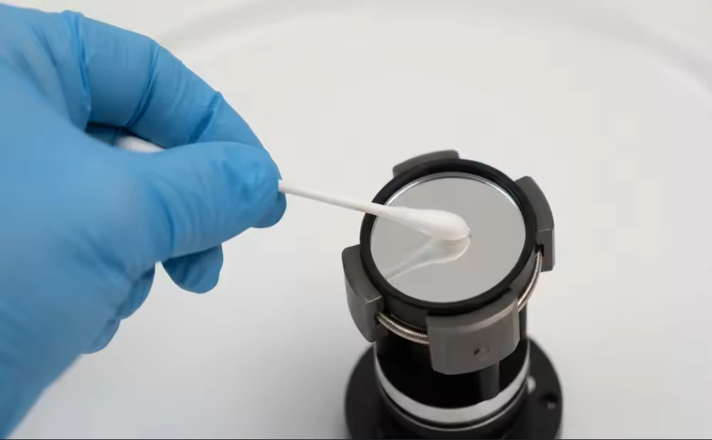 青い手袋を着用し、綿棒を使ってアイピースを掃除している技術者の様子